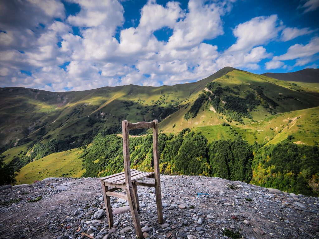a worn down wooden chair on top of a hill surrounded by green mountains