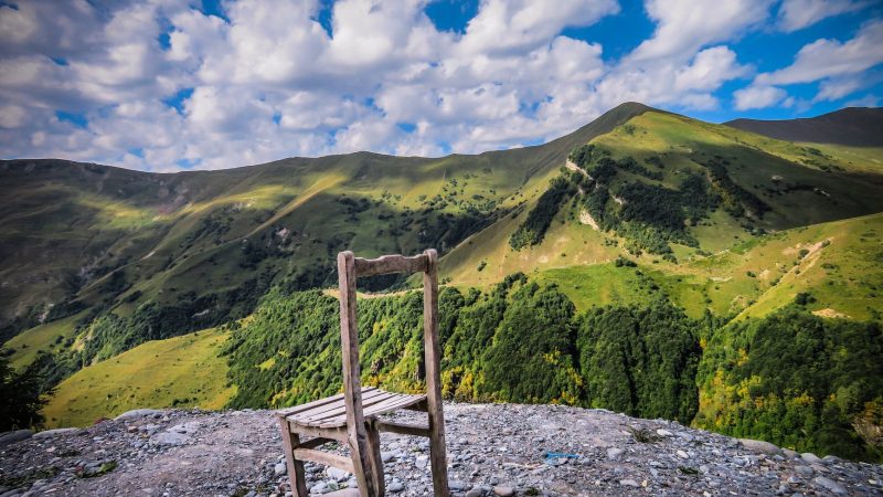 a worn down wooden chair on top of a hill surrounded by green mountains
